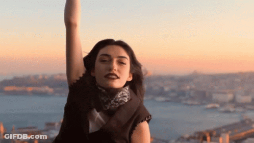 A Woman With Her Arms In The Air Looks At The Camera With A City In The Background GIF
