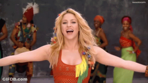 A Woman With Her Arms Outstretched In Front Of A Group Of People With Shakiragifs On The Bottom Right GIF