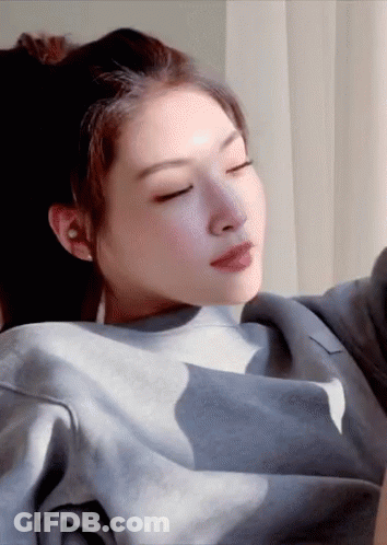 A Woman With Her Eyes Closed Is Wearing A Grey Sweater GIF