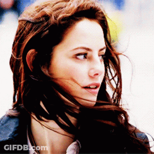 A Woman With Her Hair Blowing In The Wind Looks At The Camera GIF