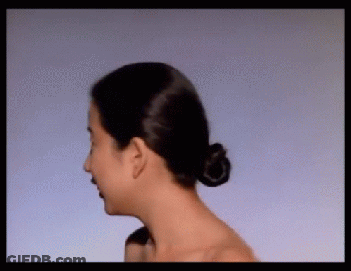 A Woman With Her Hair In A Bun Is Looking At Something GIF