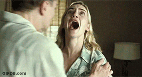 A Woman With Her Mouth Open Is Being Held By A Man In A Room . GIF