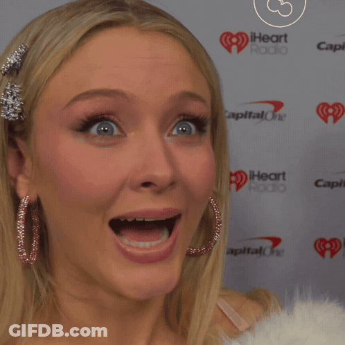 A Woman With Her Mouth Open Is Standing In Front Of A Iheart Radio Sign GIF