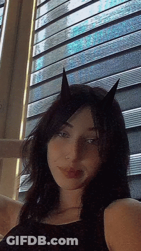 A Woman With Horns On Her Head Is Taking A Selfie In Front Of A Window GIF