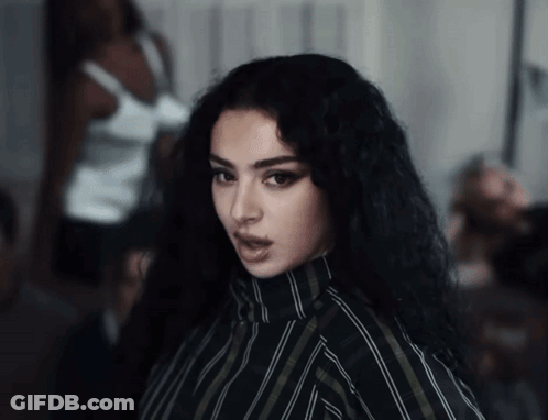 A Woman With Long Black Hair And A Striped Shirt Looks At The Camera GIF