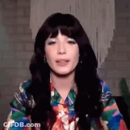 A Woman With Long Black Hair And Bangs Is Wearing A Colorful Shirt And Tie . GIF