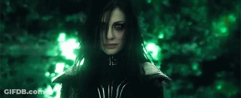 A Woman With Long Black Hair And Green Eyes Is Standing In Front Of A Forest . GIF