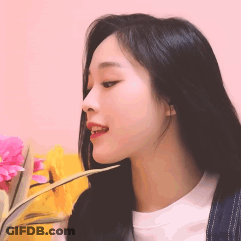 A Woman With Long Black Hair Is Holding A Flower In Her Hand GIF