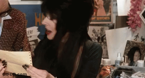 A Woman With Long Black Hair Is Holding A Piece Of Paper In Front Of A Man . GIF