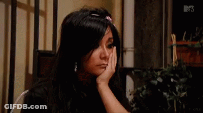 A Woman With Long Black Hair Is Sitting At A Table With Her Hand On Her Face . GIF