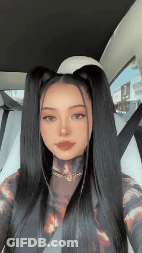 A Woman With Long Black Hair Is Sitting In A Car With A Seat Belt On . GIF