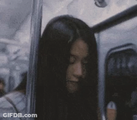 A Woman With Long Black Hair Is Sitting On A Bus And Looking At The Camera . GIF