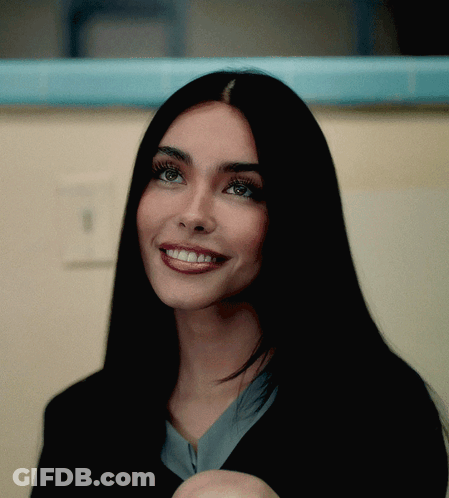 A Woman With Long Black Hair Is Smiling And Looking At The Camera GIF
