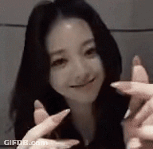 A Woman With Long Black Hair Is Smiling And Making A Peace Sign With Her Fingers . GIF