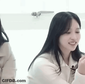 A Woman With Long Black Hair Is Smiling While Sitting Next To Another Woman In A Room . GIF