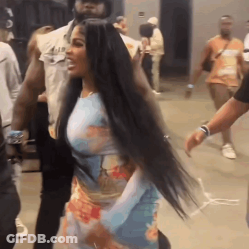 A Woman With Long Black Hair Is Standing In A Crowd . GIF