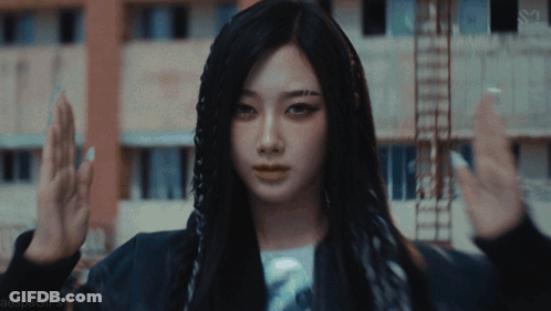 A Woman With Long Black Hair Is Standing In Front Of A Building With Her Hands In The Air GIF