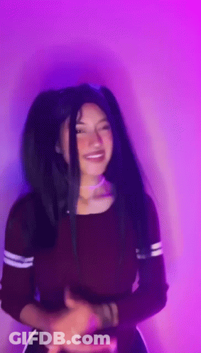 A Woman With Long Black Hair Is Standing In Front Of A Purple Wall . GIF