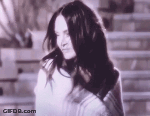 A Woman With Long Black Hair Is Standing In Front Of A Staircase . GIF