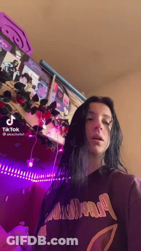 A Woman With Long Black Hair Is Standing In Front Of A Wall With Purple Lights . GIF