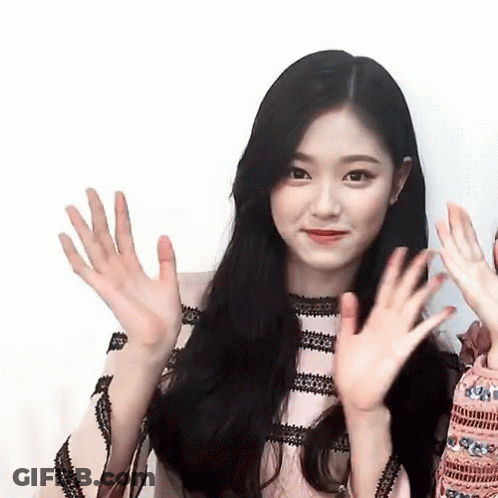 A Woman With Long Black Hair Is Waving Her Hands At The Camera . GIF