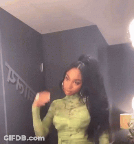 A Woman With Long Black Hair Is Wearing A Green Dress And A Ponytail . GIF