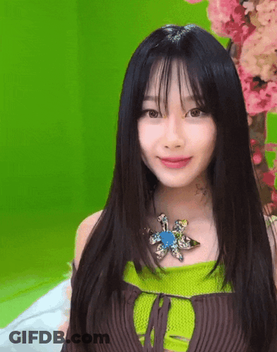 Woman With Black Hair Green Top And Flower Necklace GIF