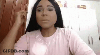 A Woman With Long Black Hair Is Wearing A Pink Shirt And Applying Makeup To Her Face . GIF