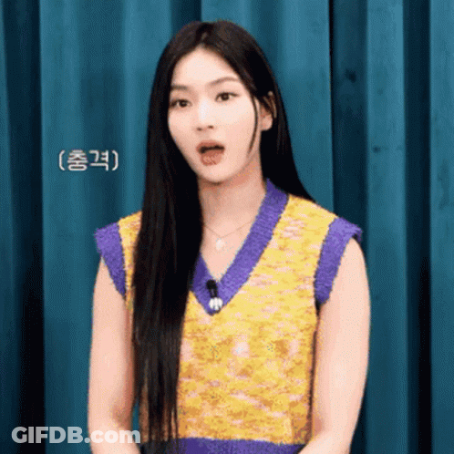 A Woman With Long Black Hair Is Wearing A Purple And Yellow Vest . GIF