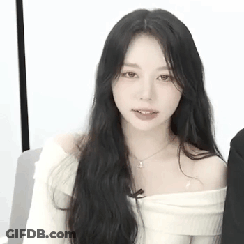 A Woman With Long Black Hair Is Wearing A White Off The Shoulder Sweater And Necklace . GIF