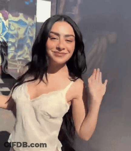 A Woman With Long Black Hair Is Wearing A White Tank Top And Smiling GIF