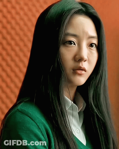 A Woman With Long Black Hair Wearing A Green Sweater And White Shirt GIF