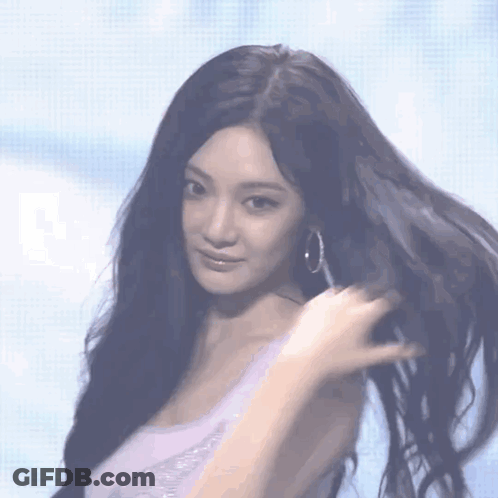A Woman With Long Black Hair Wearing Hoop Earrings Looks At The Camera GIF
