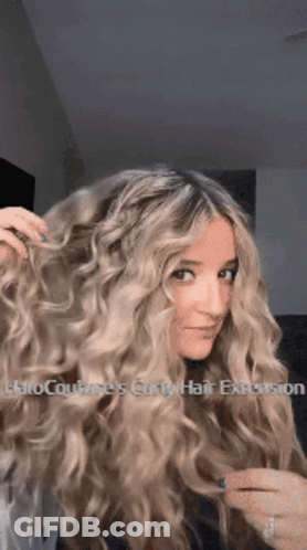 A Woman With Long Blonde Curly Hair Has A Halo Couture 'S Curly Hair Extension In Her Hair . GIF