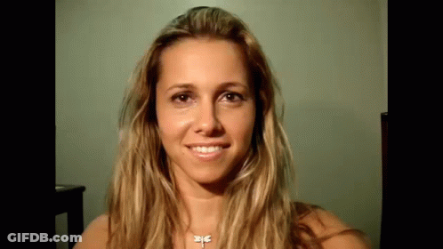 A Woman With Long Blonde Hair And A Dragonfly Necklace Is Smiling . GIF
