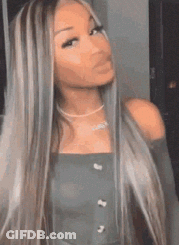 A Woman With Long Blonde Hair And A Necklace Is Standing In Front Of A Mirror And Looking At The Camera . GIF