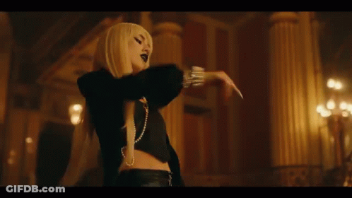A Woman With Long Blonde Hair And A Pearl Necklace Is Standing In A Dark Room With Her Arms Outstretched . GIF