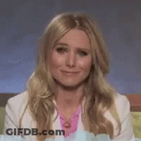 A Woman With Long Blonde Hair And A White Jacket Is Smiling . GIF