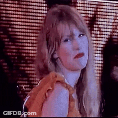 A Woman With Long Blonde Hair And Red Lips Is Making A Funny Face In Front Of A Curtain . GIF