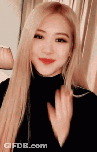 A Woman With Long Blonde Hair And Red Lips Is Wearing A Black Turtleneck And Waving . GIF