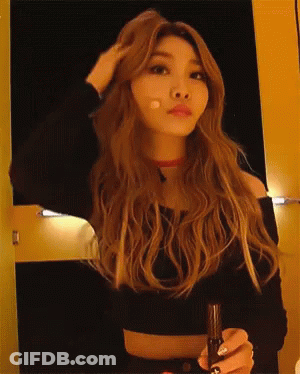 A Woman With Long Blonde Hair Is Holding A Microphone And Adjusting Her Hair GIF