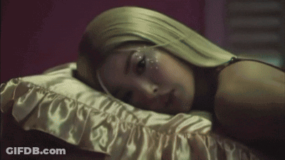 A Woman With Long Blonde Hair Is Laying On A Bed GIF