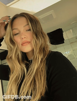 A Woman With Long Blonde Hair Is Looking At The Camera GIF
