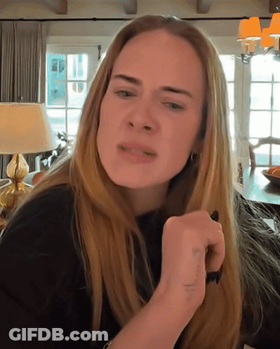 A Woman With Long Blonde Hair Is Making A Funny Face In A Living Room GIF