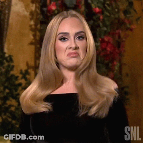 A Woman With Long Blonde Hair Is Making A Funny Face While Standing In Front Of Flowers . GIF