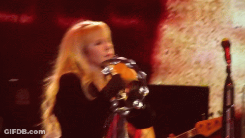 A Woman With Long Blonde Hair Is Playing A Tambourine On A Stage GIF