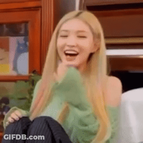 A Woman With Long Blonde Hair Is Sitting On A Couch Laughing With Her Mouth Open . GIF