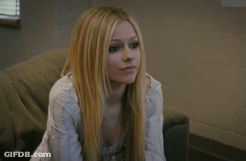 A Woman With Long Blonde Hair Is Sitting On A Couch Looking At The Camera GIF