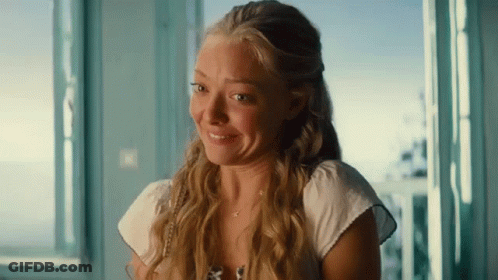 A Woman With Long Blonde Hair Is Smiling And Looking Out Of A Window GIF