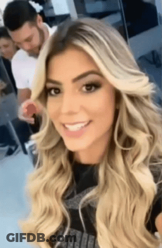 A Woman With Long Blonde Hair Is Smiling And Taking A Selfie GIF